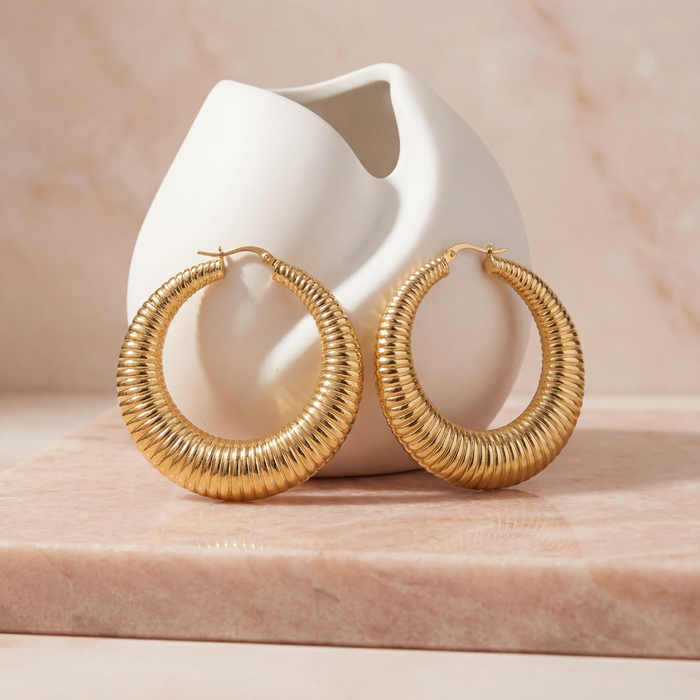 Large 50mm gold textured hoop earrings with a bold hammered finish, statement hoop earrings photographed on a blush stone surface.