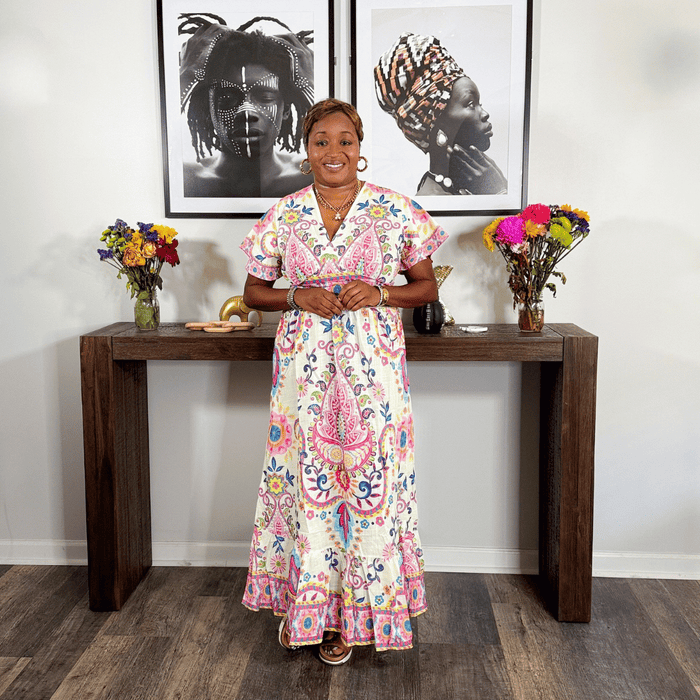 Woman in a floral dress standing in a room with a wooden console table and framed art on the wall.