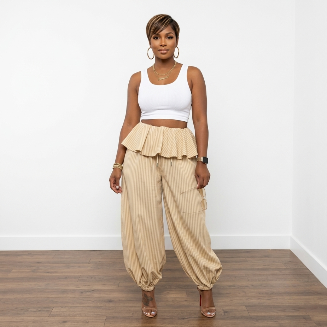 Woman wearing a white top and light yellow pinstripe high-waisted pants with ruffled details on a plain background