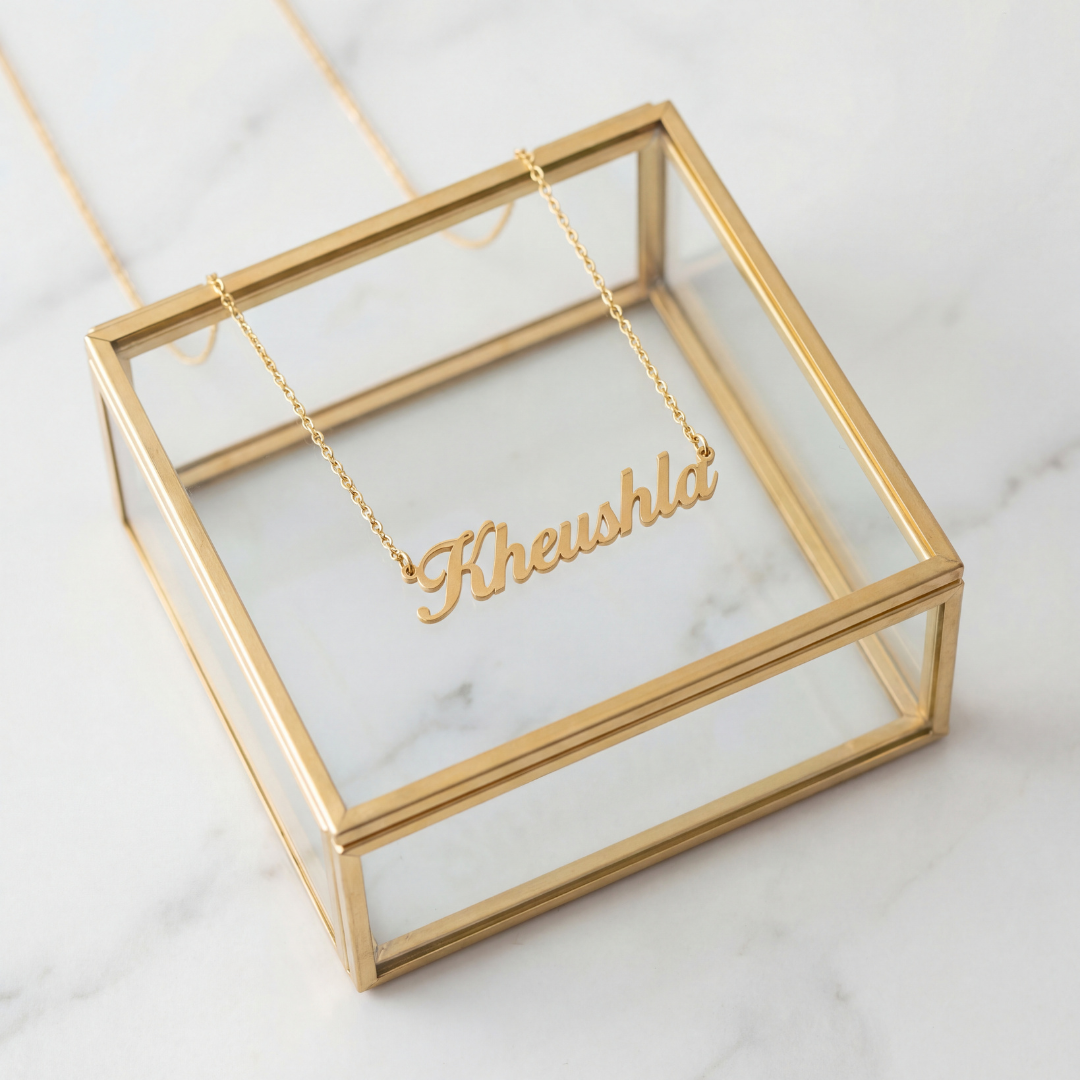 gold cursive personalized name necklace spelling Kheushla displayed on a glass jewelry box on white marble