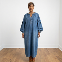 Model wearing the Lena Denim Dress, showing its loose fit, button-front details, and long lantern sleeves in a white room with hardwood flooring.