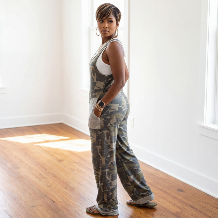 Woman wearing a camouflage jumpsuit in a bright room with wooden floor and white walls.