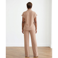 African American woman wearing a mocha two-piece shirt and pants set with a button-down top and wide-leg pants in a white room with hardwood floors