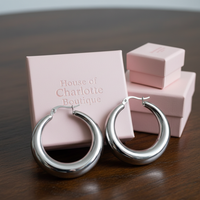 Amelia 1.5-inch silver statement hoop earrings displayed on a pink House of Charlotte Boutique jewelry box on a dark wood table