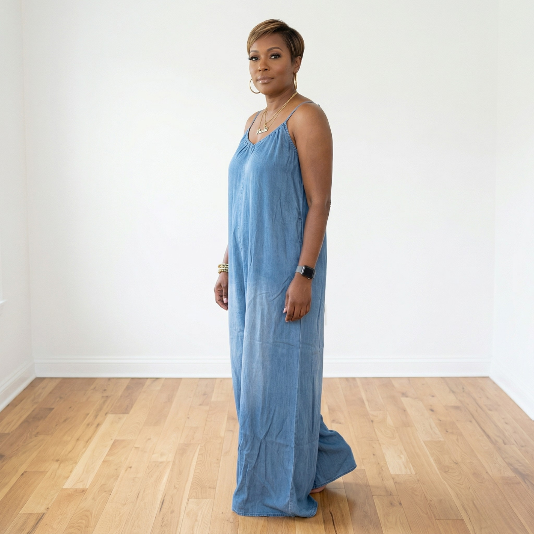 Side view of African American woman wearing Maizey denim chambray sleeveless wide leg jumpsuit showing relaxed fit and flowy leg silhouette