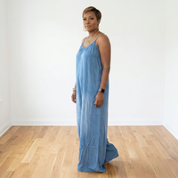Side view of African American woman wearing Maizey denim chambray sleeveless wide leg jumpsuit showing relaxed fit and flowy leg silhouette