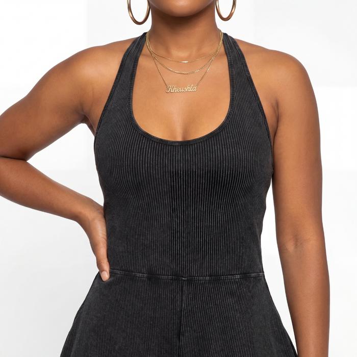 Woman wearing a black ribbed jumpsuit with gold jewelry on a white background