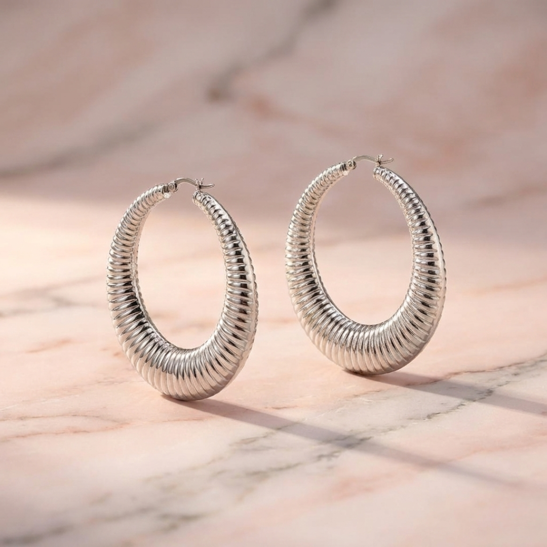 Large 50mm silver textured hoop earrings with a bold textured design, oversized statement hoops styled on a minimalist blush background.