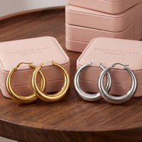 Side-by-side comparison of Amelia 1.5-inch statement hoop earrings in gold and silver on pink House of Charlotte Boutique jewelry boxes