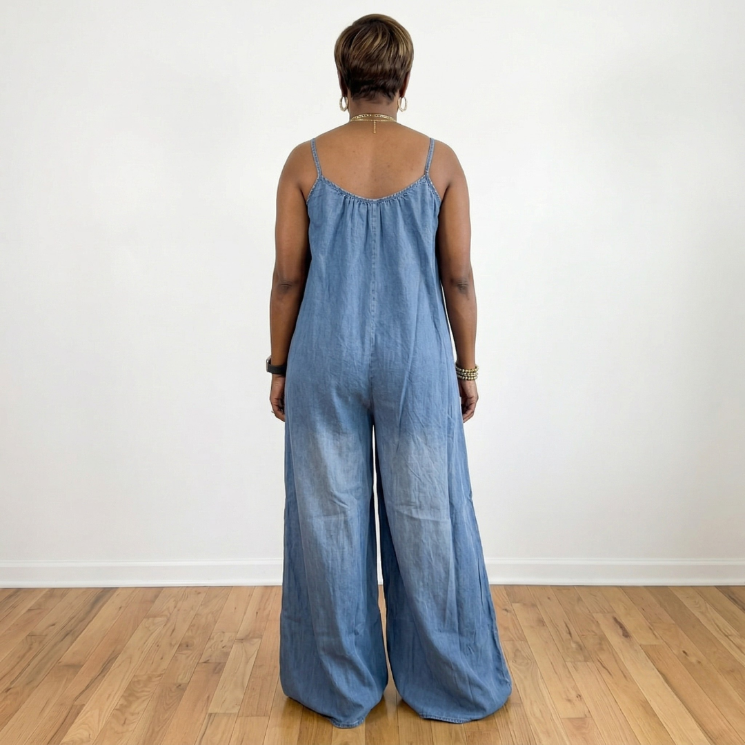 Back view of African American woman wearing Maizey denim chambray wide leg jumpsuit with adjustable straps and loose fit design