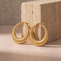 Medium 40mm gold textured hoop earrings with a dimensional hammered finish, versatile statement hoops styled on a blush stone surface.