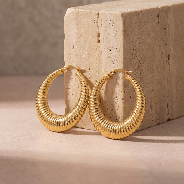 Medium 40mm gold textured hoop earrings with a dimensional hammered finish, versatile statement hoops styled on a blush stone surface.