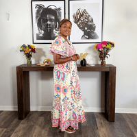 Woman in a colorful dress standing in a room with a wooden console table and framed art on the wall.