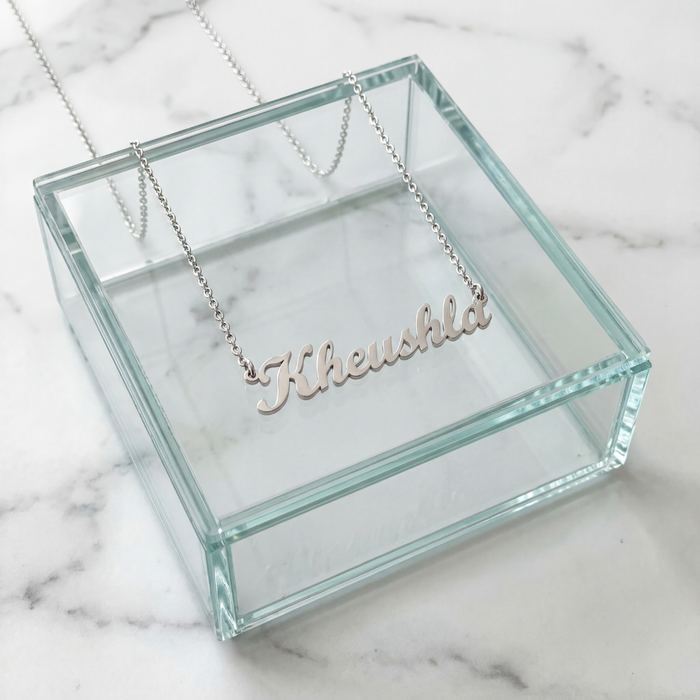Silver cursive personalized name necklace spelling Kheushla displayed on a glass jewelry box on white marble