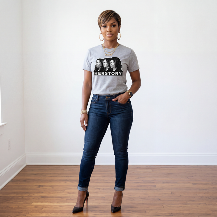 Woman wearing a t-shirt with 'HERSTORY' design and dark jeans in a room.