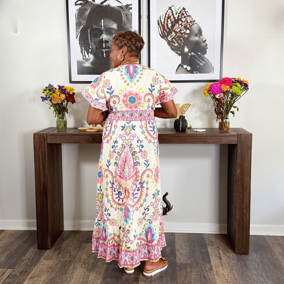 Woman in a colorful dress standing at a wooden console table with floral arrangements.