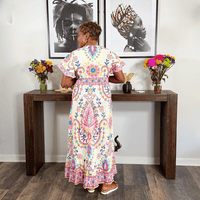 Woman in a colorful dress standing at a wooden console table with floral arrangements.