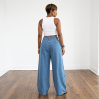 Person wearing a white crop top and blue wide-leg jeans on a wooden floor with a white wall background