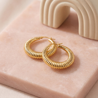 Small 33mm gold textured hoop earrings with a subtle hammered finish, lightweight everyday hoops photographed on a blush stone surface.