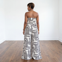 Woman wearing a strapless, patterned jumpsuit standing on a wooden floor with a white wall background.
