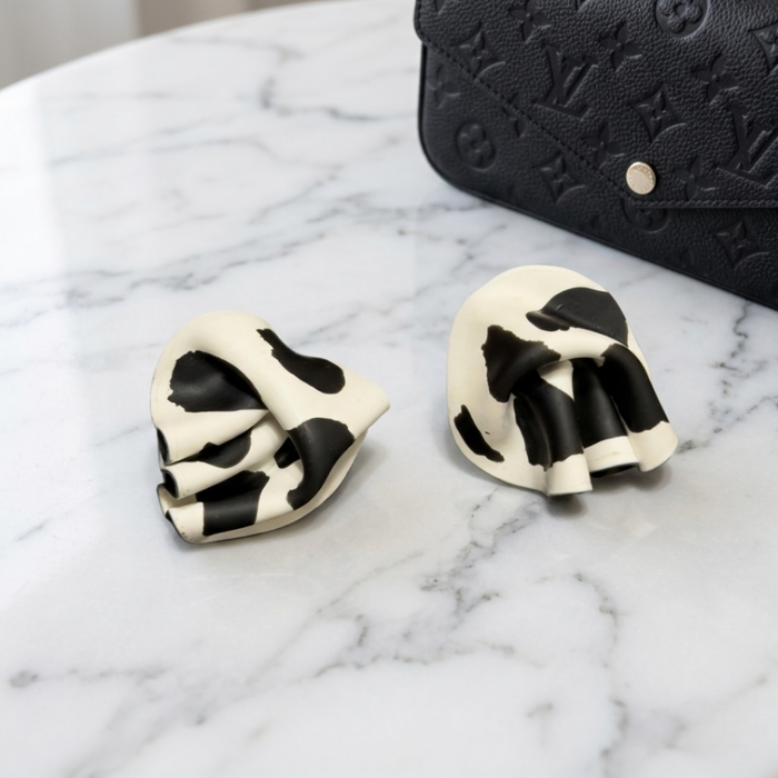 Black and white earrings on a marble surface with a black handbag in the background